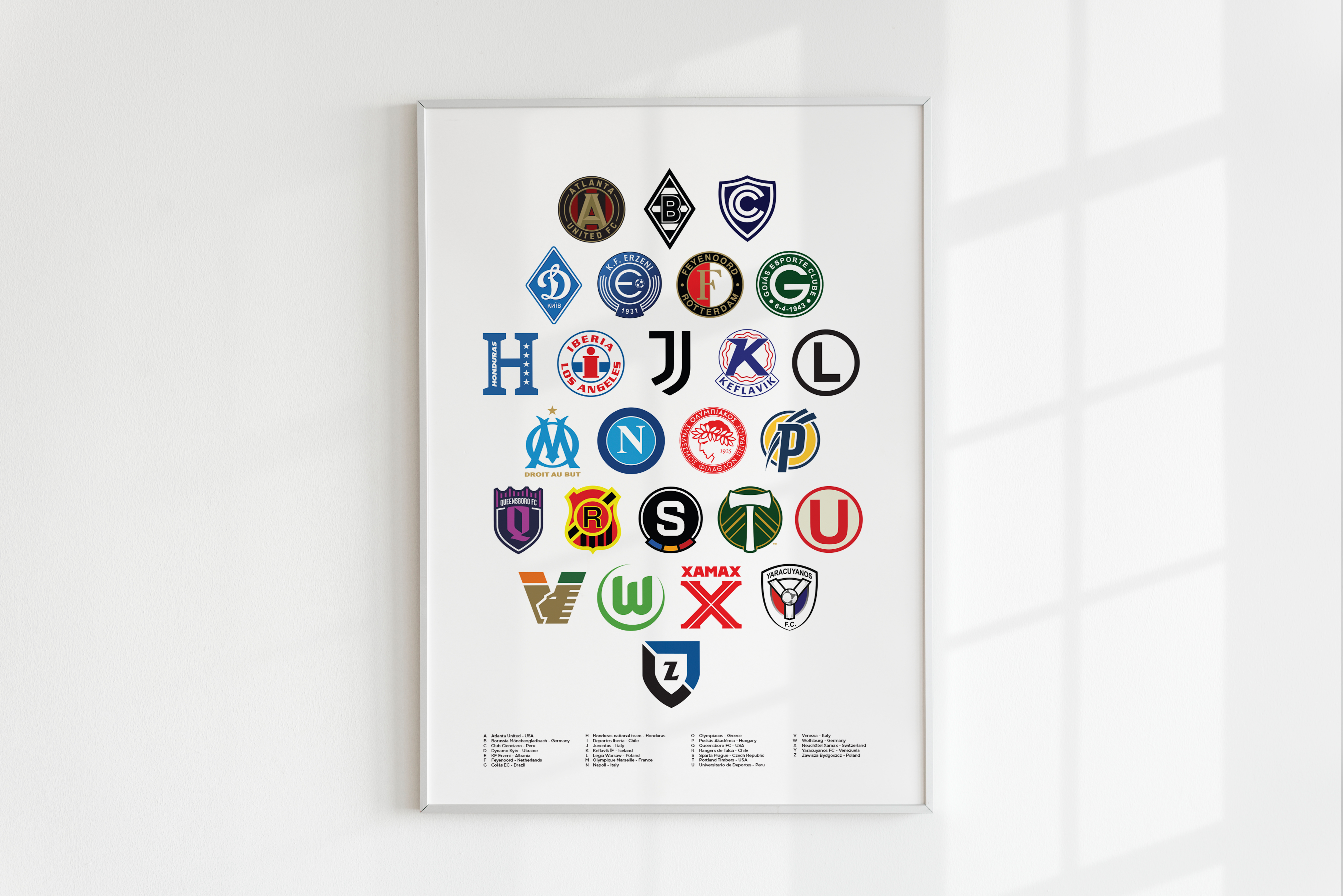 Football Alphabet poster framed in white hanging on a white background featuring 26 Football clubs from all over the world. Each football logo represents each letter of the alphabet